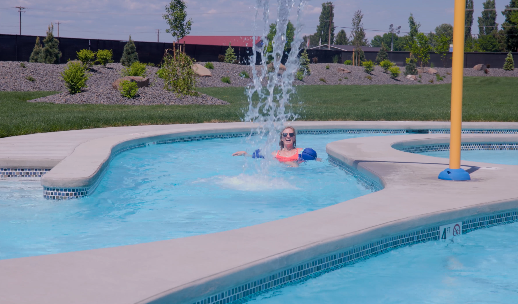 A woman floating down the Legends outdoor pool lazy river, nearing the waterfall feature where she will be doused with cool cascading water.