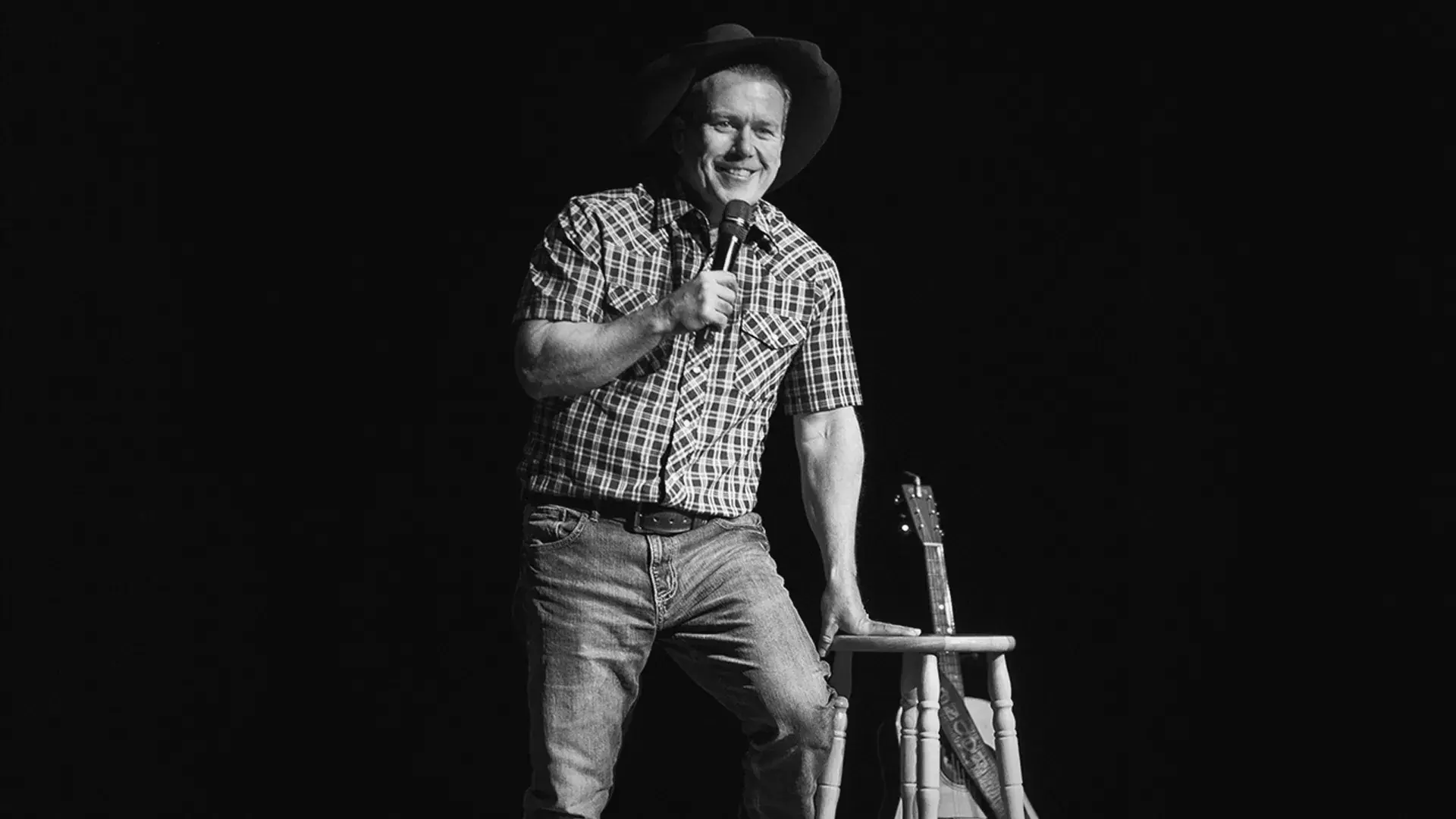 Rodney Carrrington in black and white on stage leaning against a barstool